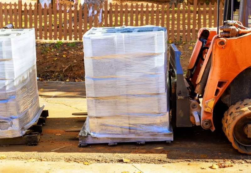 Worker unloads concrete blocks for retaining wall from pallet while using small tractor